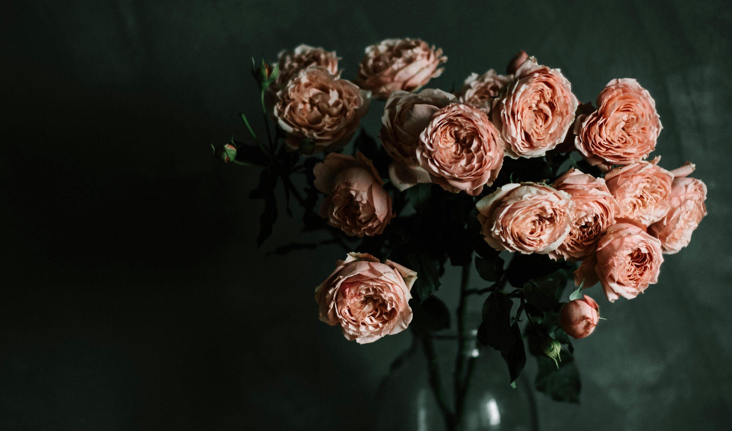 A bouquet of fresh cut flowers beside a glass jar filled with rose petals for skincare.