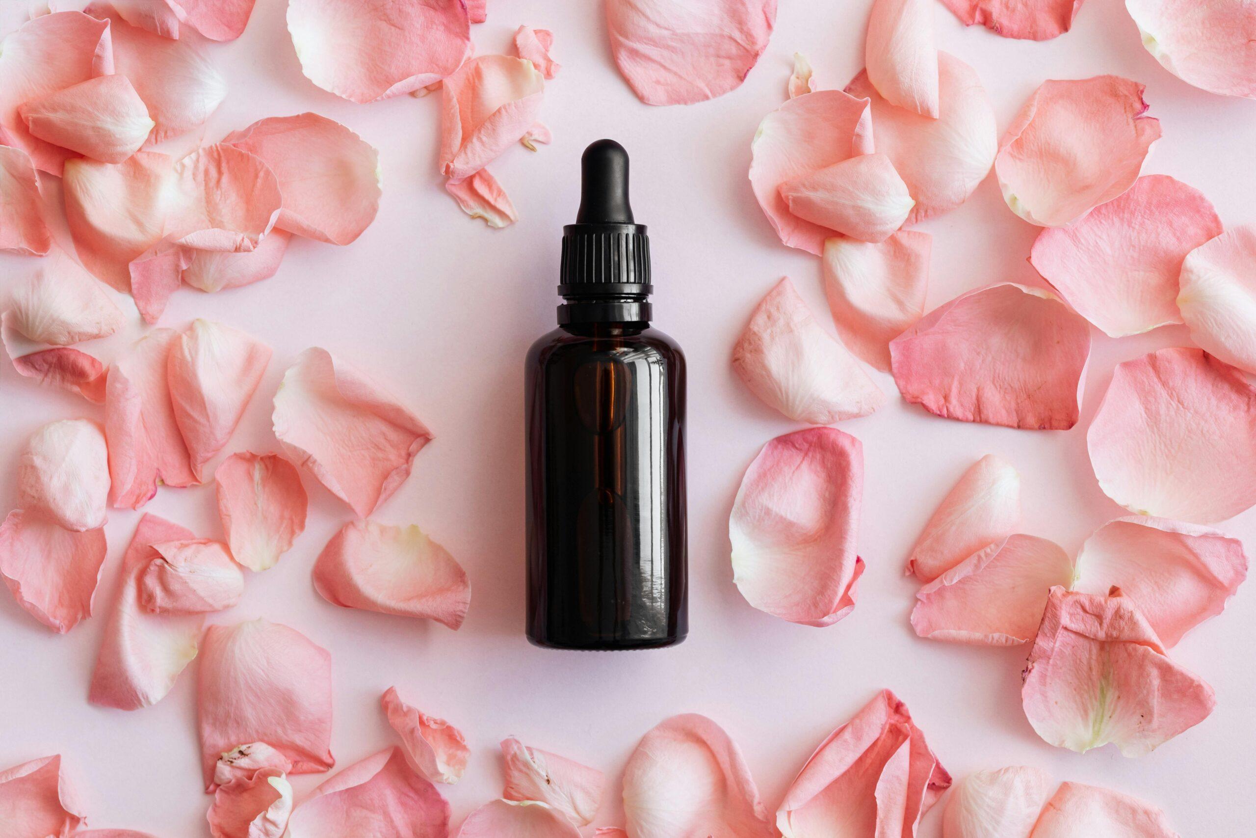 A glowing woman smiling confidently while holding a glass jar filled with dried rose petals and essential oils.