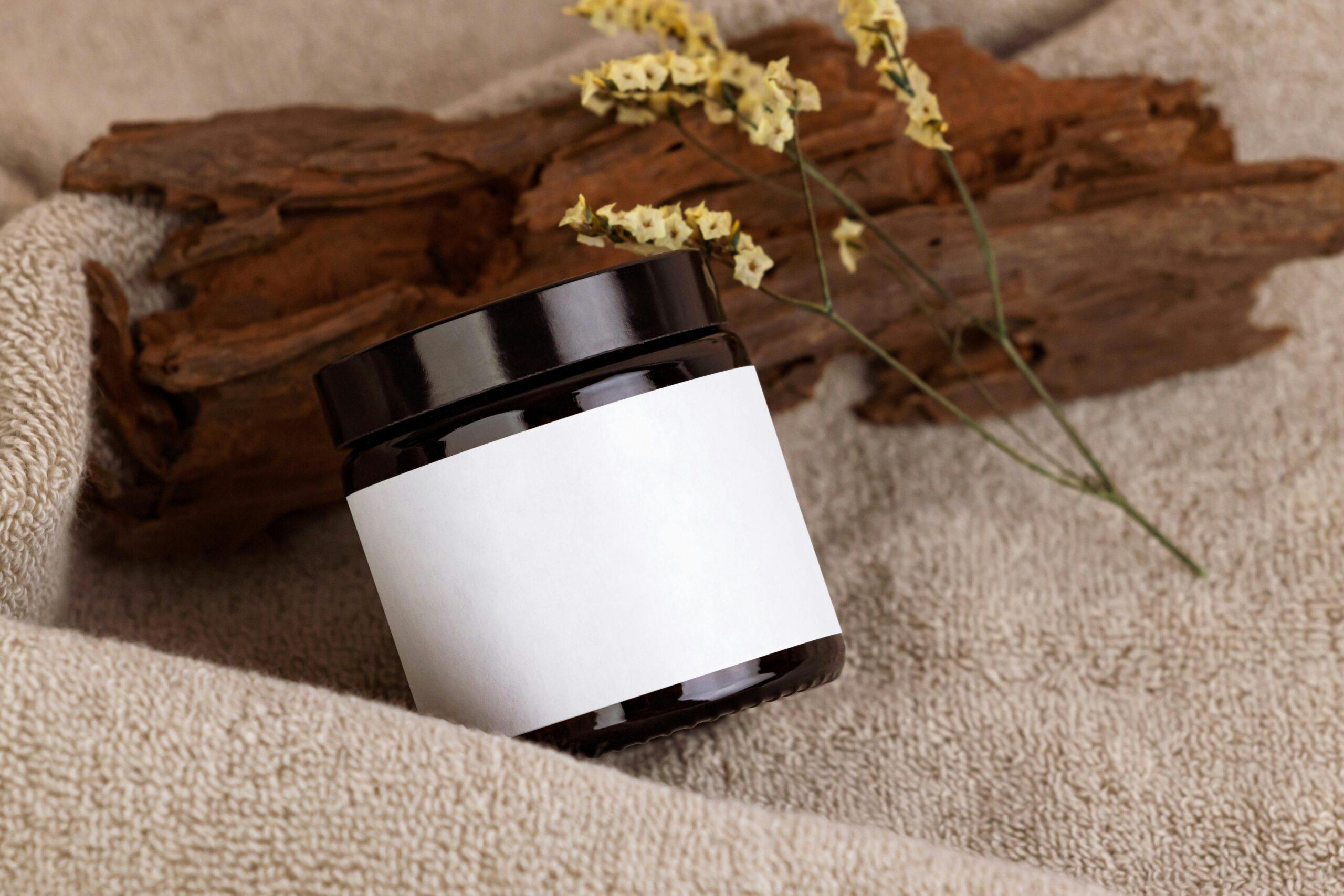 A wooden table displaying various jars of herbal skincare products, surrounded by dried flowers and handwritten labels.