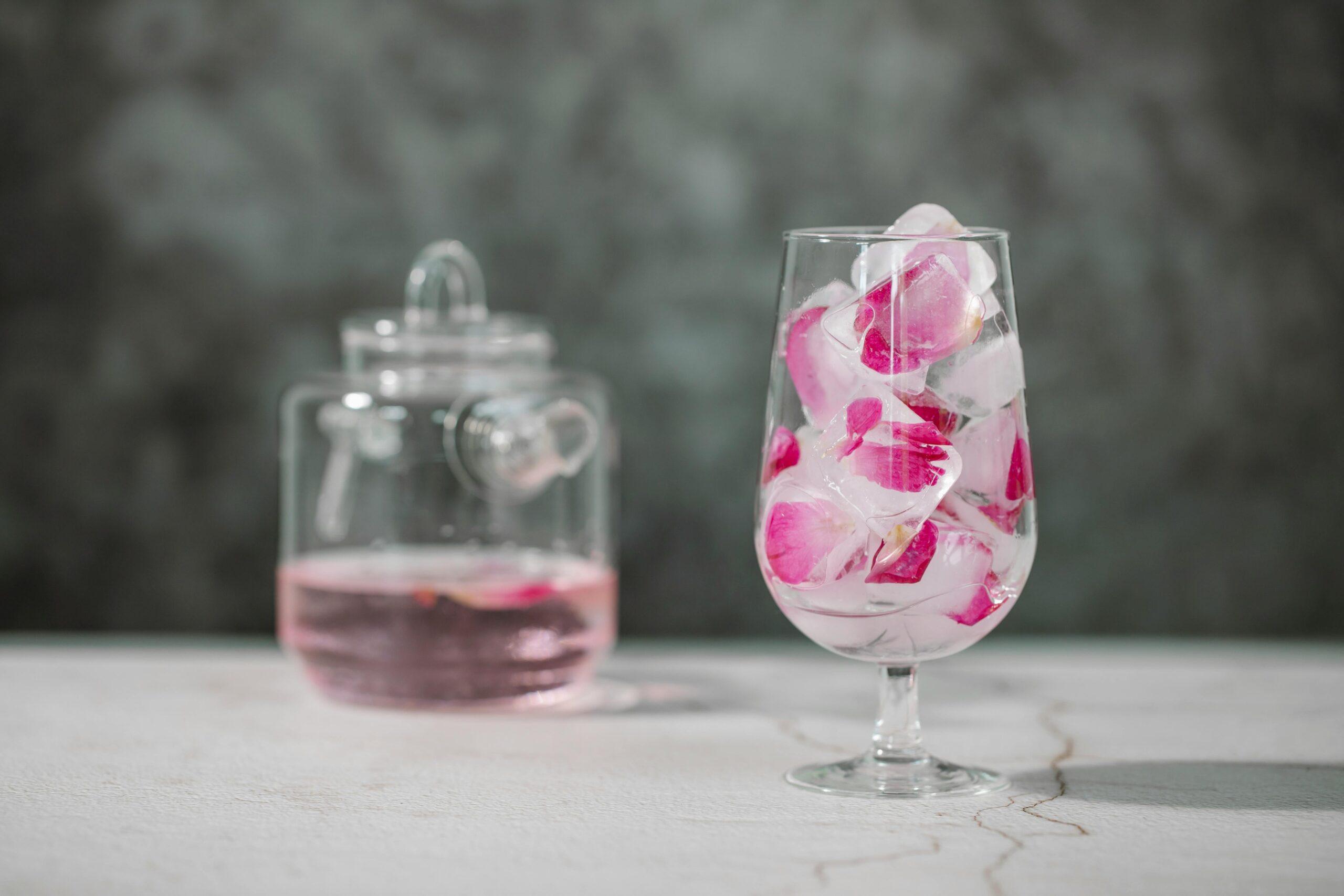 A glass jar filled with rose-infused water sitting beside fresh rose petals