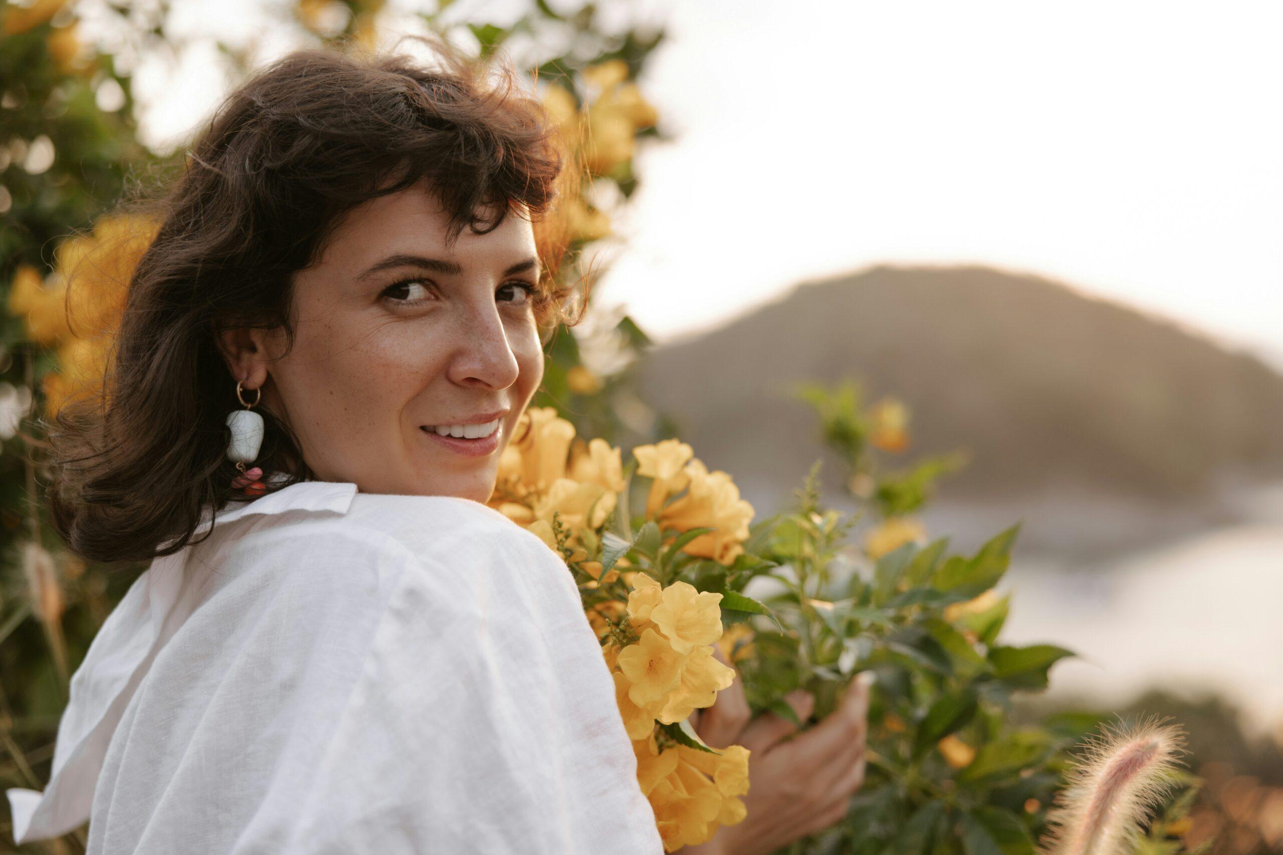 A smiling woman holding a colorful box filled with fresh organic flowers next to a handwritten note.