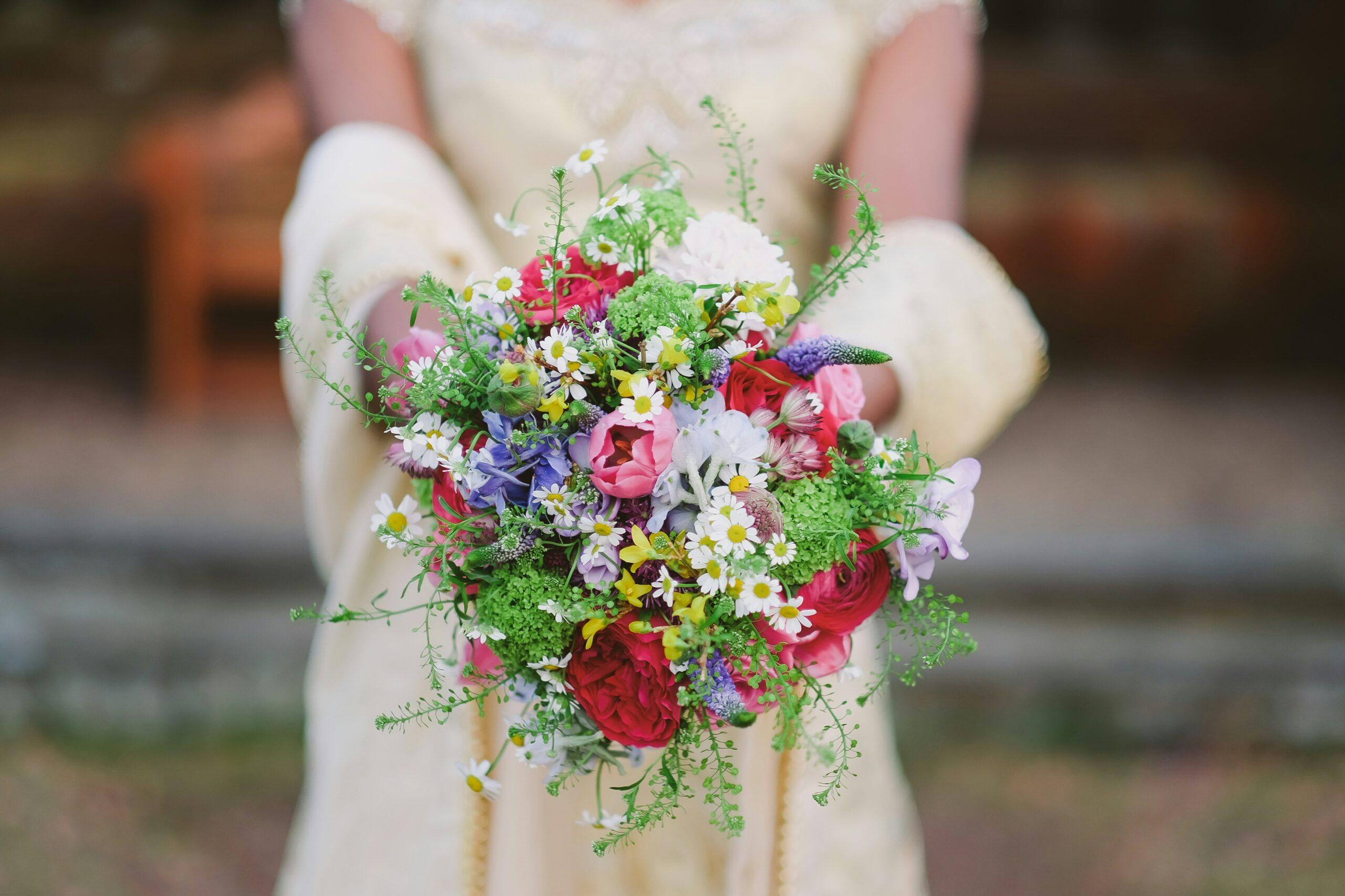 An elegant bride holding a rustic yet stylish organic wedding bouquet featuring sunflowers and wildflowers.
